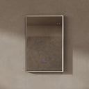 BAI 21030 modern rectangular 24-inch wall-mounted mirror with a slim LED light that's off with gold frame, shown against a textured beige wall. The mirror has small control touch sensor dots near the bottom center.