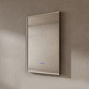 BAI 21030 modern rectangular 24-inch wall-mounted mirror with a slim LED light that's currently off with gold frame, shown against a textured beige wall. The mirror has small control touch sensor dots near the bottom center.