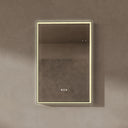 BAI 21030 modern rectangular 24-inch wall-mounted mirror with a slim warm LED light with gold frame, shown against a textured beige wall. The mirror has small control touch sensor dots near the bottom center.