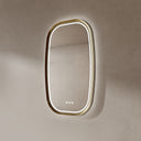 BAI 21041 modern oval wall-mounted vanity bathroom led mirror with a slim gold frame and integrated LED lighting, shown against a textured beige wall with white front and side lighting.