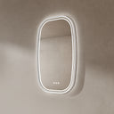 BAI 21042 modern oval LED-backlit wall bathroom mirror with a white frame and illuminated border, mounted on a textured beige plaster wall side view.