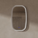 BAI 21042 modern oval LED-backlit wall bathroom mirror with a white frame and illuminated border, mounted on a textured beige plaster wall with the lights off.