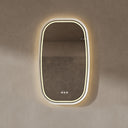 BAI 21042 modern oval LED-backlit wall bathroom mirror with a white frame and illuminated border, mounted on a textured beige plaster wall with warm lighting.