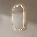 BAI 21042 modern oval LED-backlit wall bathroom mirror with a white frame and illuminated border, mounted on a textured beige plaster wall with warm lighting.