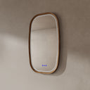 BAI 21043 modern oval wall-mounted led bathroom mirror with a light wood oak frame and integrated LED lighting, shown on a textured beige wall with the lights off side view.