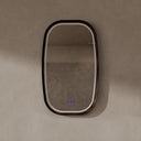 BAI 21044 modern oval LED-backlit vanity bathroom mirror with a dark wood walnut frame, mounted on a textured beige wall with lights off.