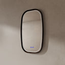 BAI 21044 modern oval LED-backlit vanity bathroom mirror with a dark wood walnut frame, mounted on a textured beige wall with lights off side view.