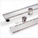 Stainless steel linear shower drain channel with a slotted bottom, shown with mounting hardware including a black rubber grommet, a metal basket strainer, and a small hook on a white background.